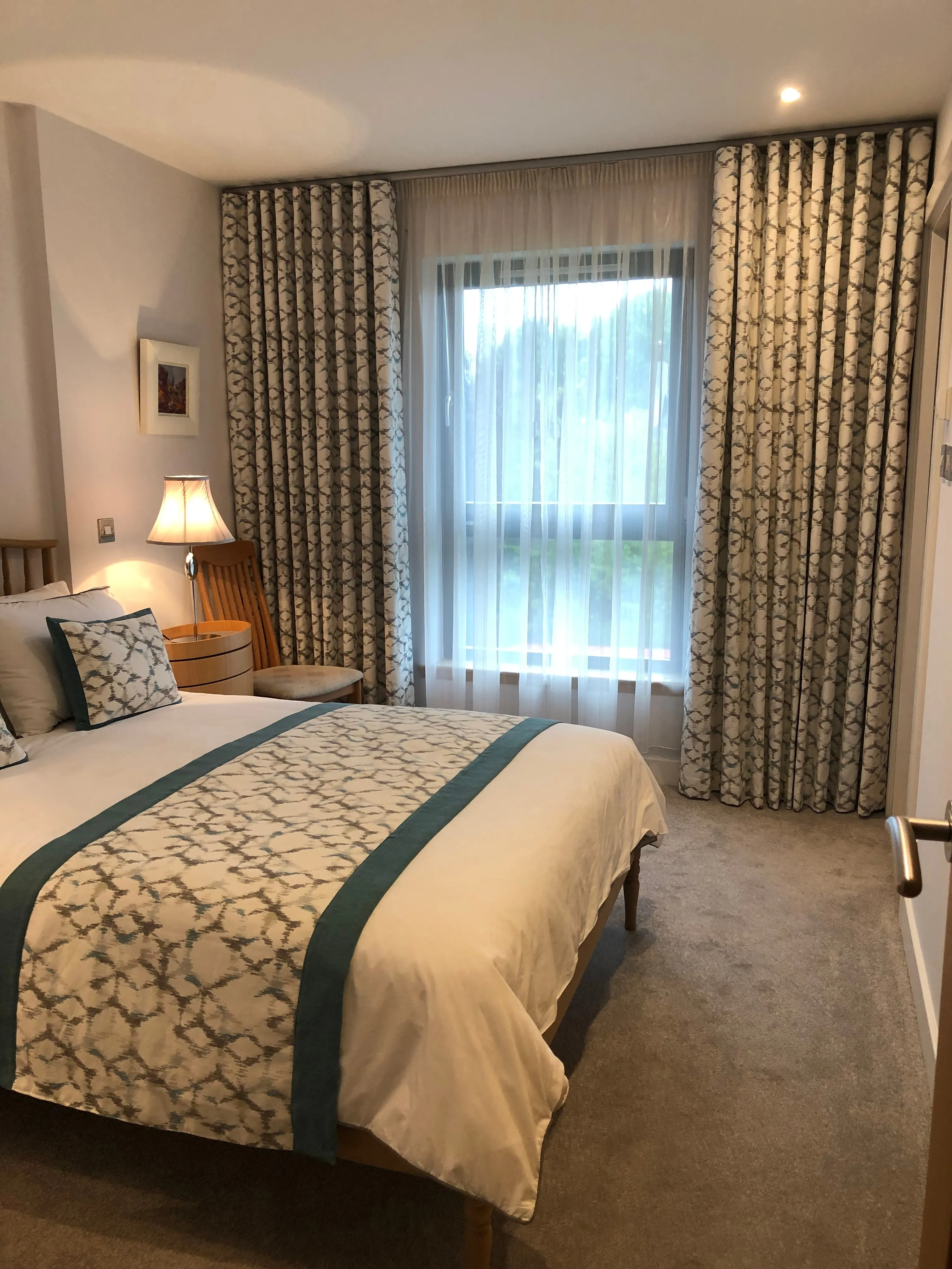 Bedroom with floor-to-ceiling patterned wave curtains and sheers either side of a window, above a bed dressed in matching fabric.