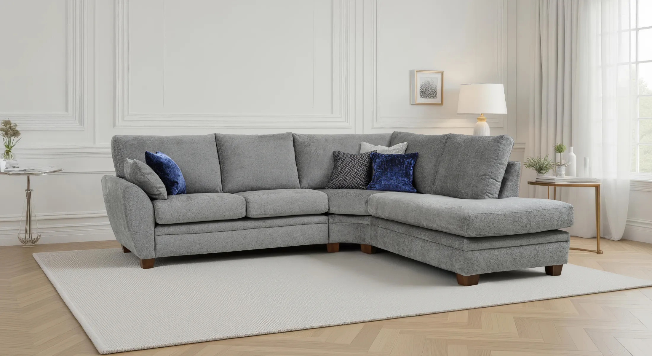 Grey chenille corner sofa with a chaise end, navy velvet and patterned accent cushions, in a panelled living room on a pale rug.